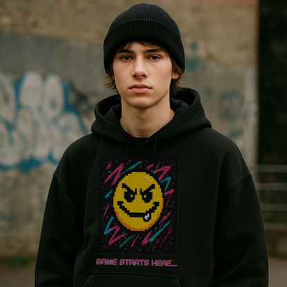 Person wearing a black hoodie with a smiley face design in front of a graffiti-covered wall.