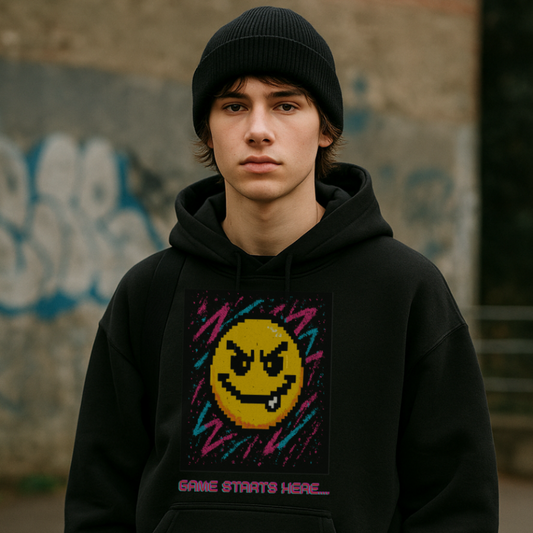 Person wearing a black hoodie with a smiley face design in front of a graffiti-covered wall.